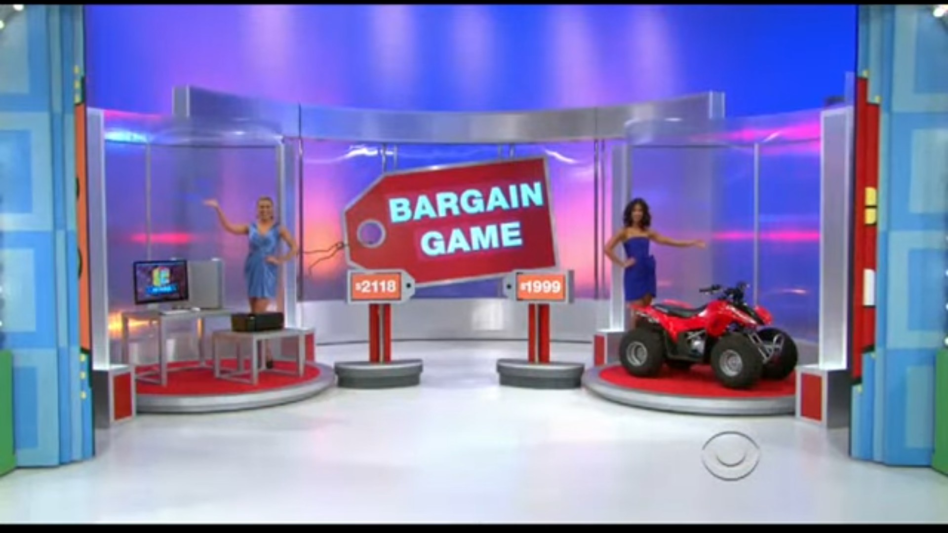 Two models display prizes for the Bargain Game on a game show set, with a red tag showing the game title and two prices beneath each prize.