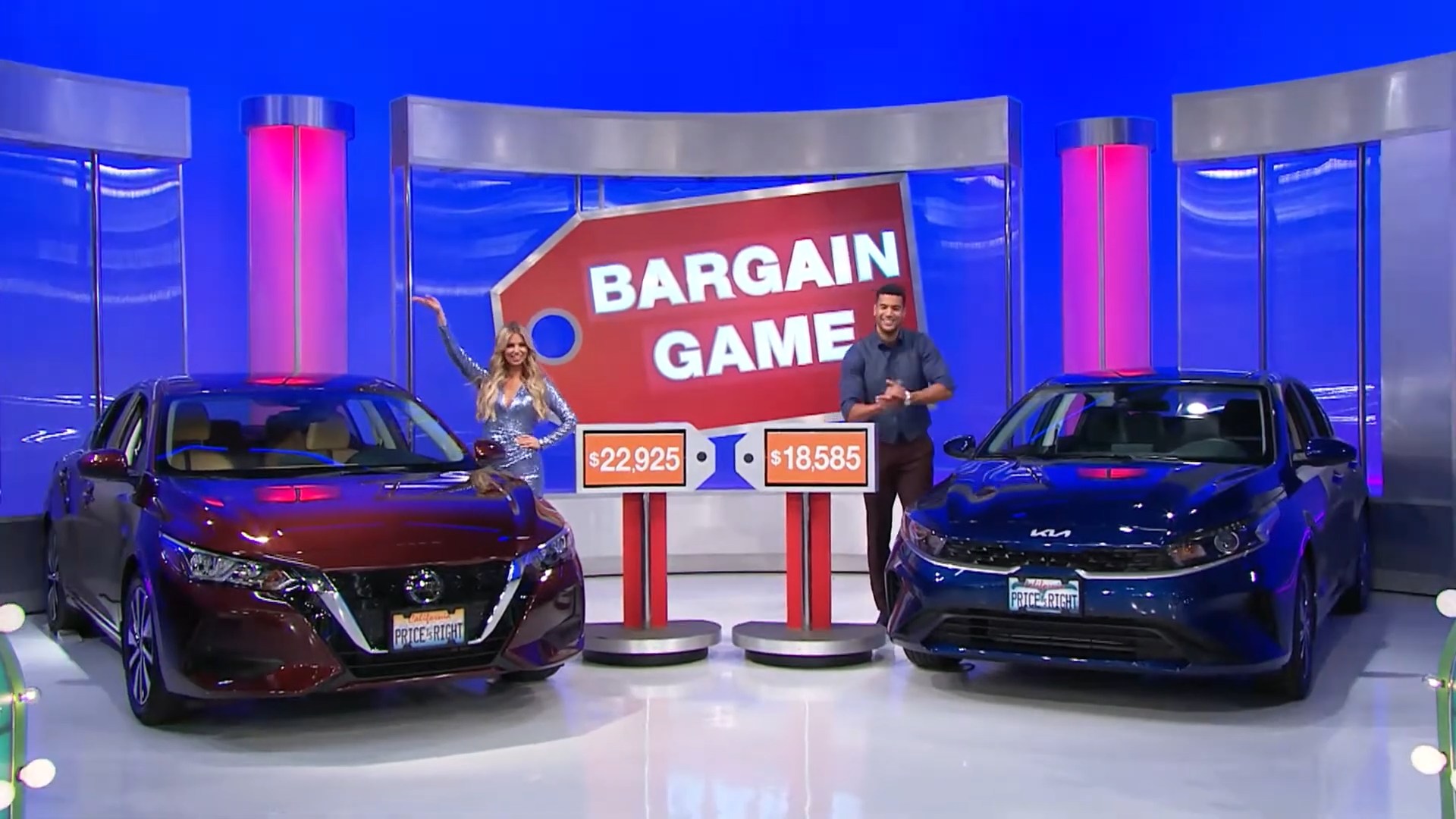 A game show scene featuring two cars on either side with their prices displayed. A female host, wearing a sparkly blue outfit, stands beside one car, and a male host claps next to the other car. A sign in the background reads 'BARGAIN GAME'.