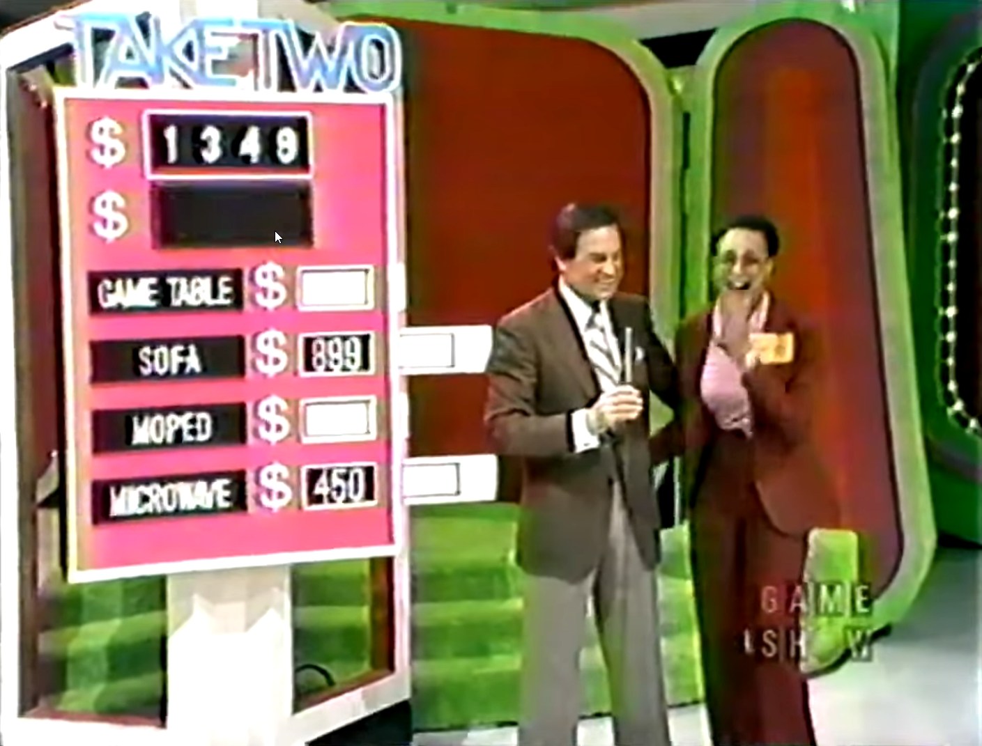 Contestant and host celebrating during the Take Two game on The Price is Right, with a scoreboard displaying a target price of 49 and prize values for game table, sofa, moped, and microwave.