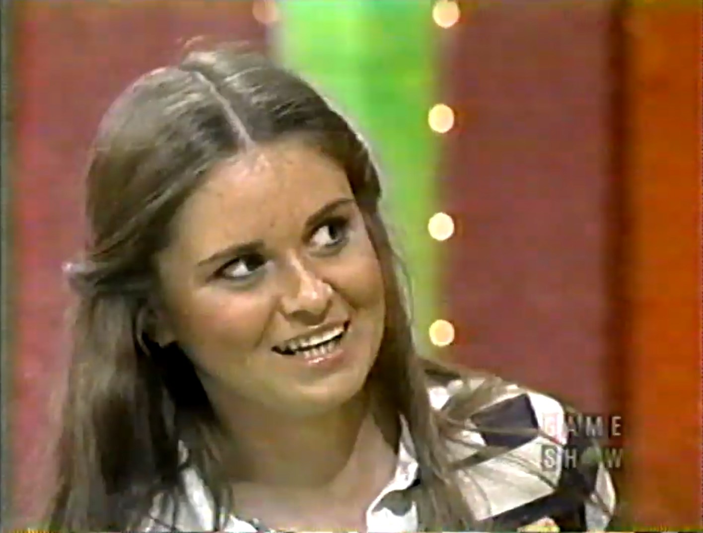 A contestant with long brown hair smiles while participating in a game show.