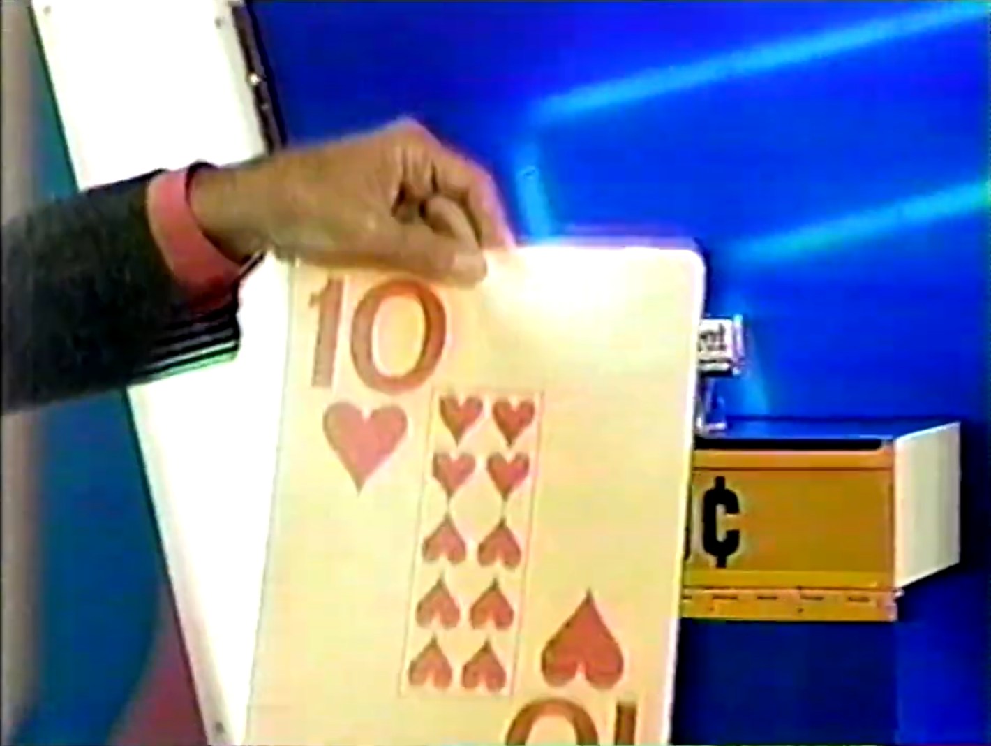 A hand holding a large card showing 10 of hearts from game show The Price is Right, with the Hit Me game board in the background.