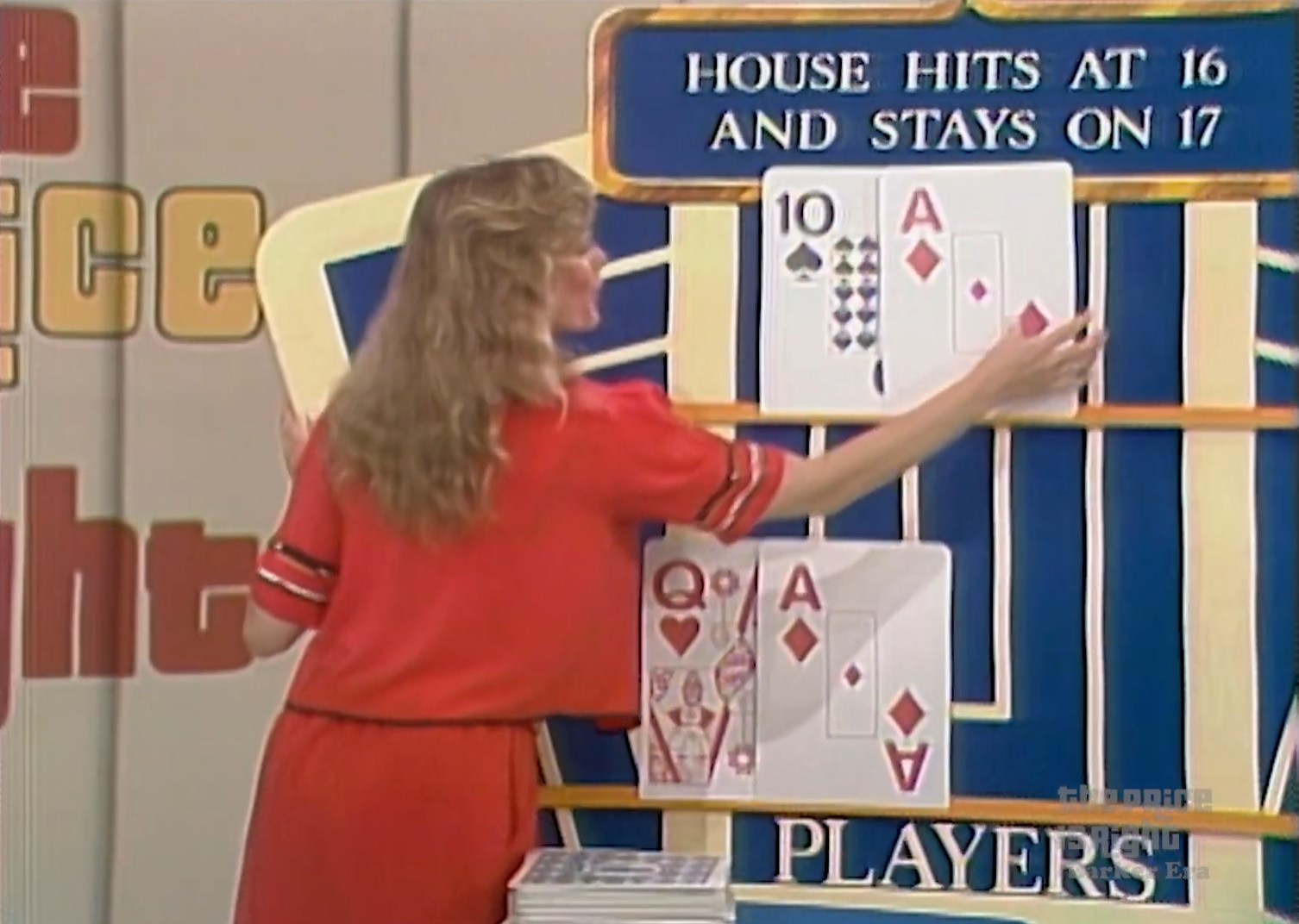 A model places an Ace of Diamonds and a 10 of Spades card on the board game 'Hit Me' on The Price is Right, showcasing that ties favor the contestant.