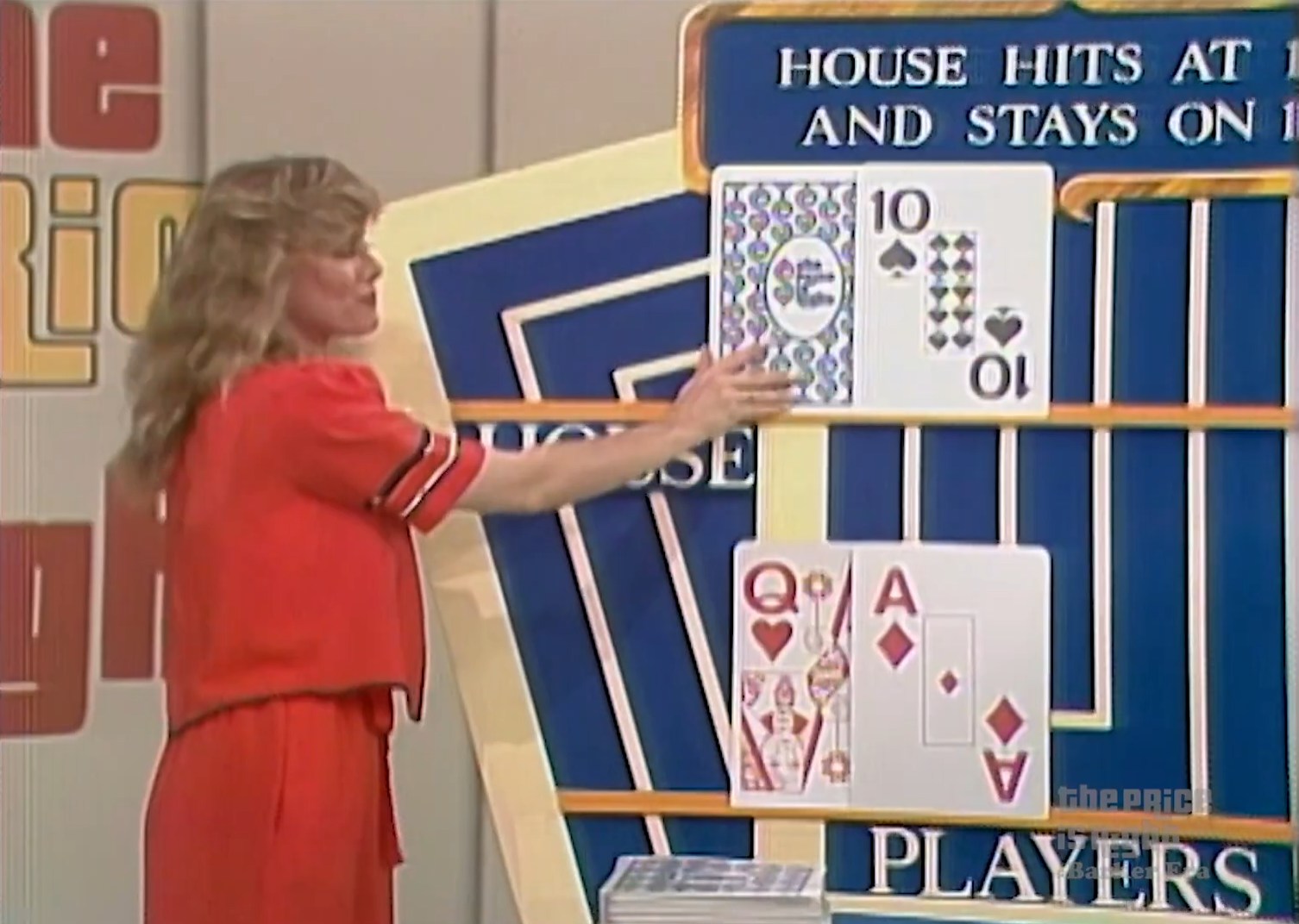 A model in a red outfit points at the house's hand in a game of 'Hit Me', showcasing a 10 of spades and a hole card. The house rules are displayed behind them.