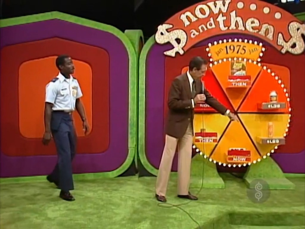 A contestant stands beside a circular game board labeled 'Now and Then', featuring prices for grocery products. The host gestures towards the board while the contestant appears to be engaged in gameplay.