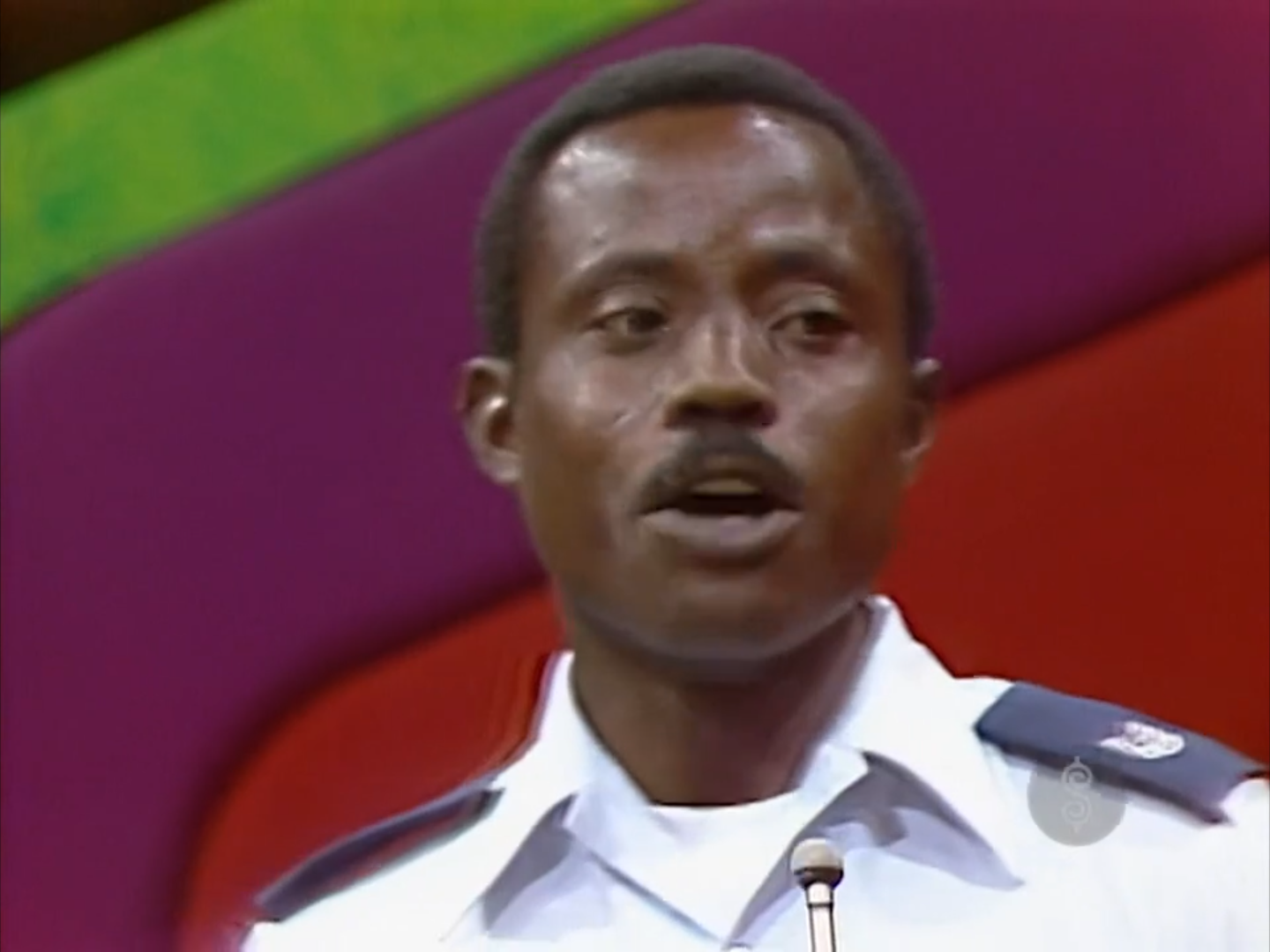 A contestant passionately speaking during a game show, with a colorful backdrop featuring purple and green.