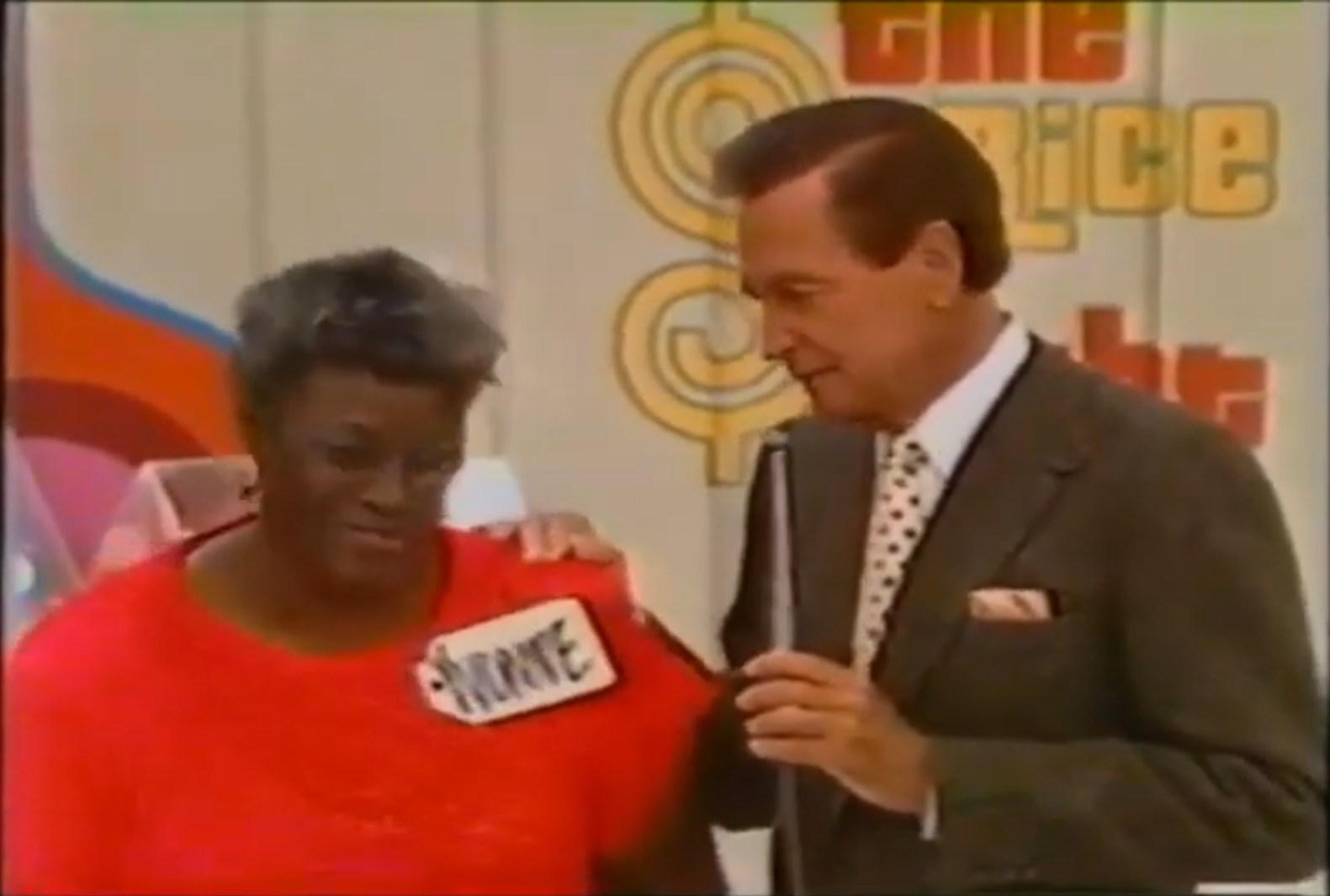 Yvonne, a contestant in a red shirt stands next to a host on the set of The Price is Right with the show's logo in the background as she prepares to play Super Ball.