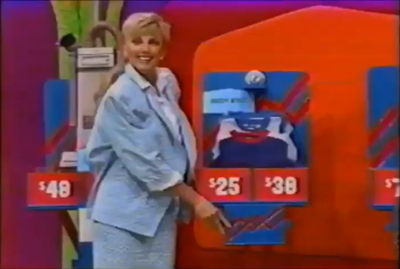 A model smiles while pointing to a price display on The Price is Right set, showcasing items with prices of  and , alongside a vacuum cleaner in the background.