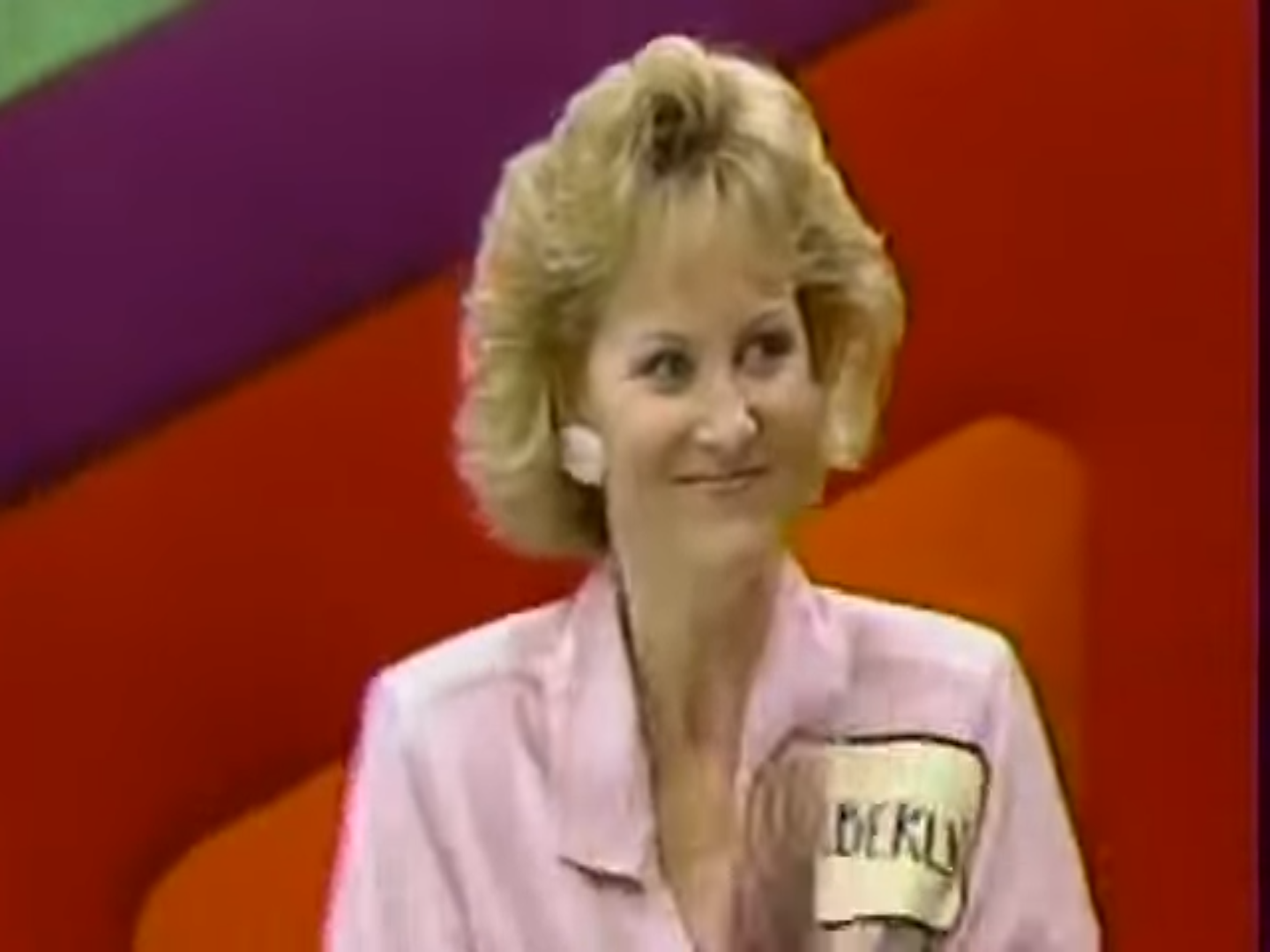 A contestant smiling and applauding during a pricing game on The Price is Right, wearing a pink outfit and a name tag.
