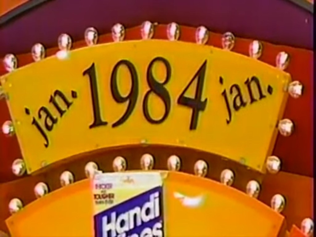 A colorful sign displaying 'jan. 1984' in bold letters, with lights surrounding it and a product labeled 'Handi-Wipes' partially visible below.