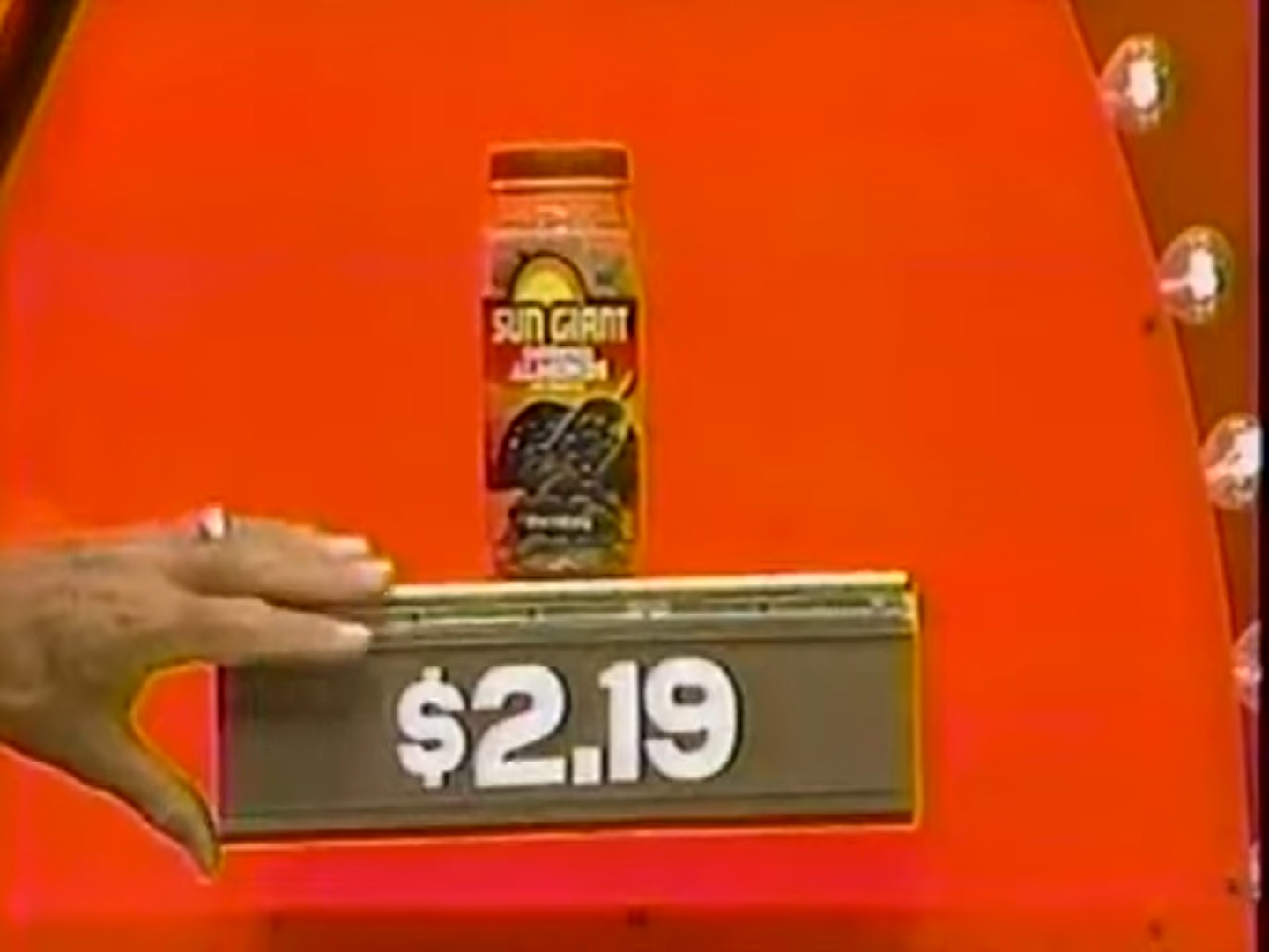 A jar of Sun Giant apricot brand fruit on a podium showing the price of .19, with a hand partially obscuring the base.