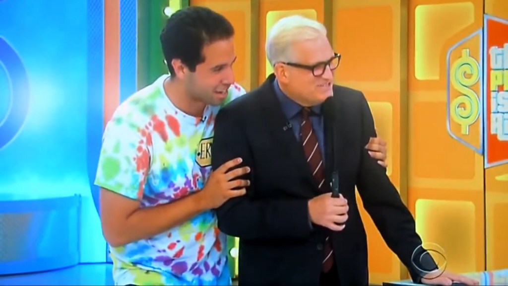 A contestant and the host of The Price is Right share a friendly moment on stage, with vibrant colorful backdrop.