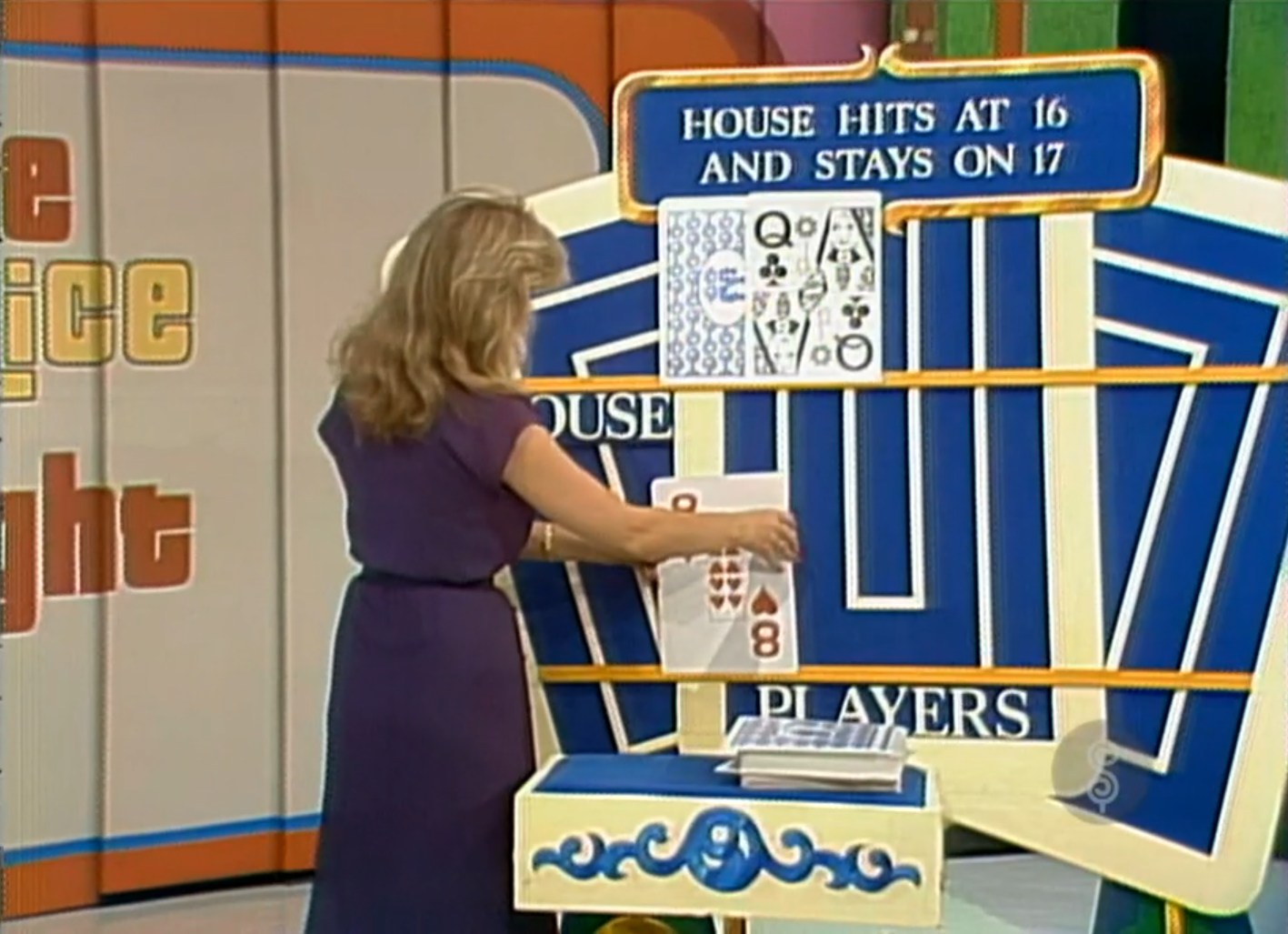 A model in a purple dress places an 8 of hearts card on a game board that shows the house's hand and scoring rules for a pricing game similar to Blackjack.