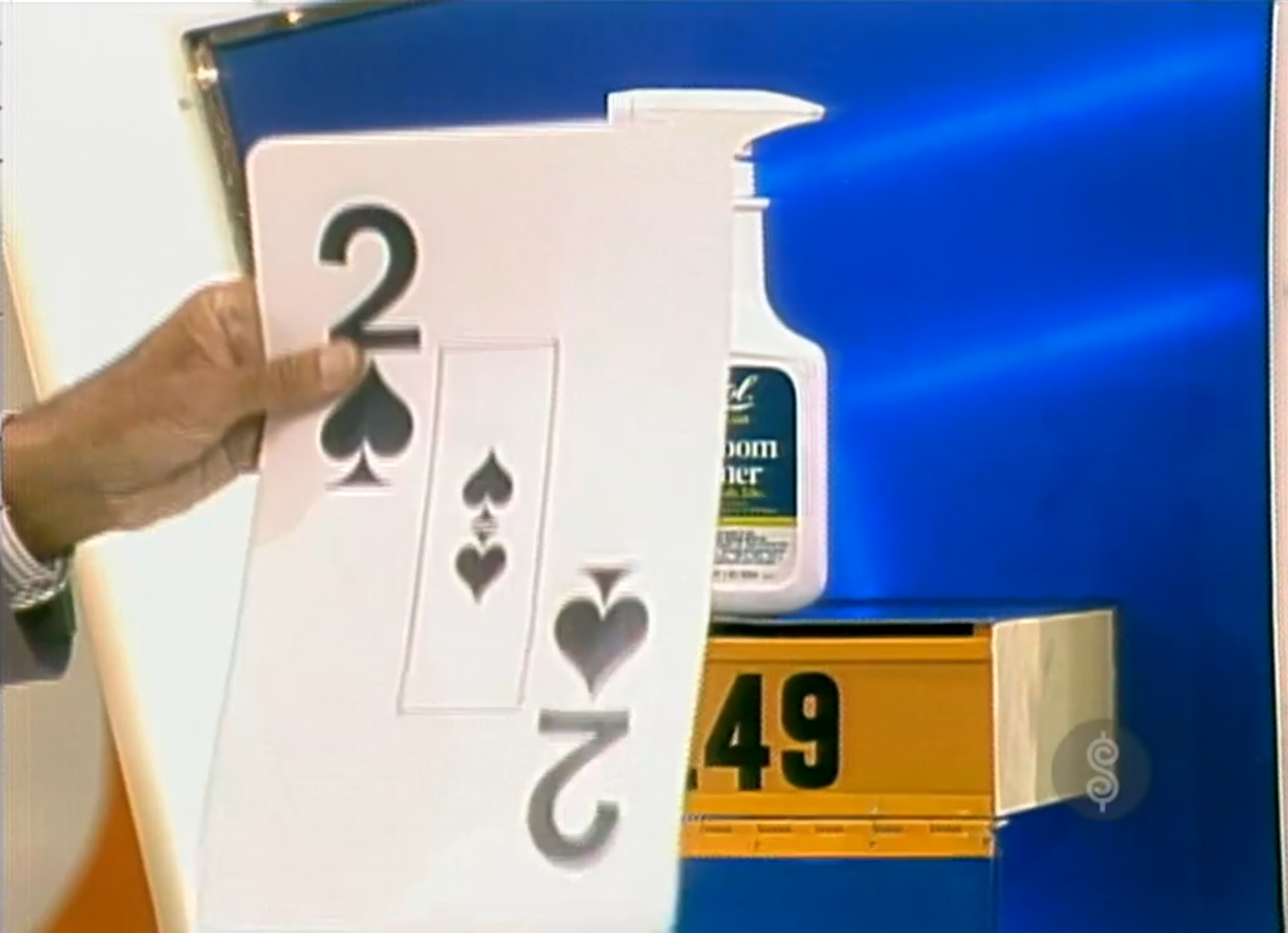 A hand holding a card displaying the number 2 of spades, next to a lotion bottle and a displayed price of .49.