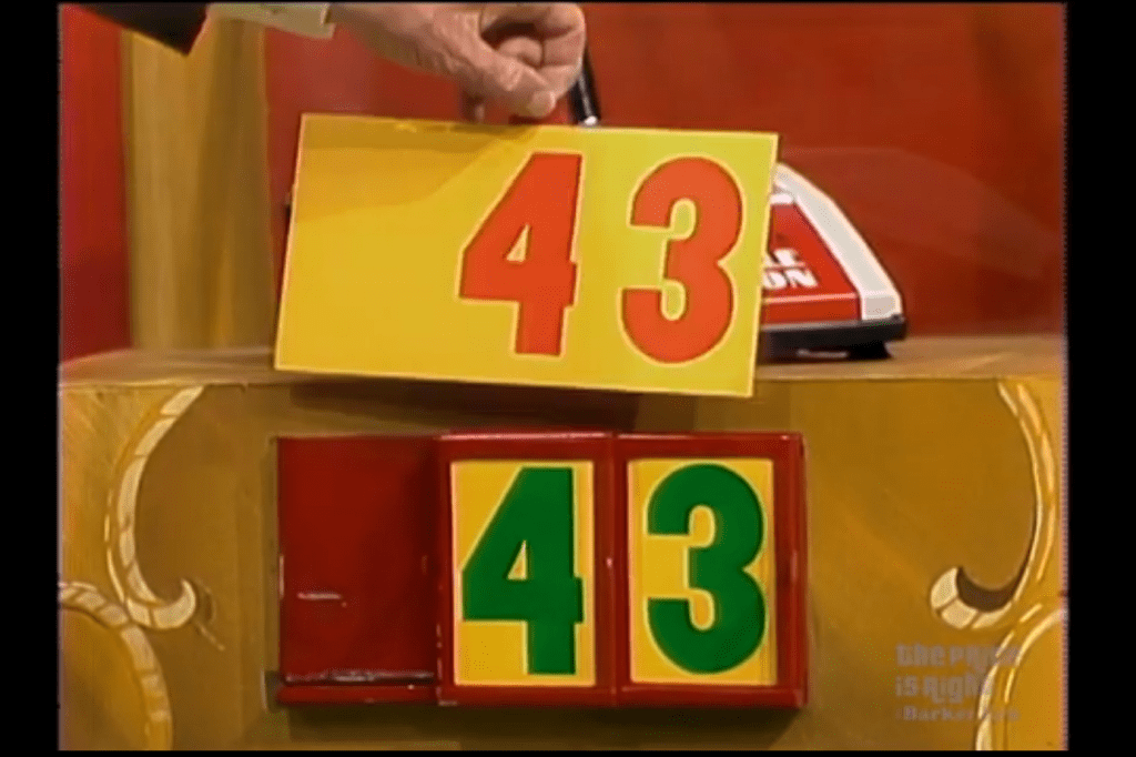 A contestant displays a price tag of , holding a large yellow card with red numbers above a game board showing the same price in green, during the 'Master Key' game.