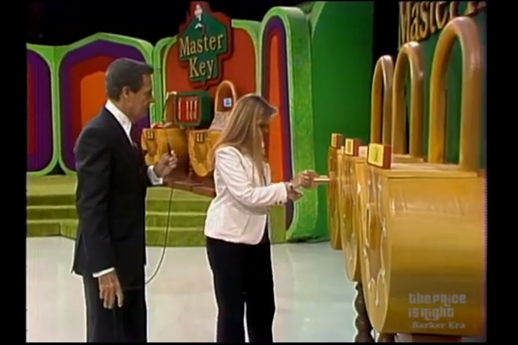 A contestant using a key on one of three locks in the Master Key game on The Price is Right, with the host observing.