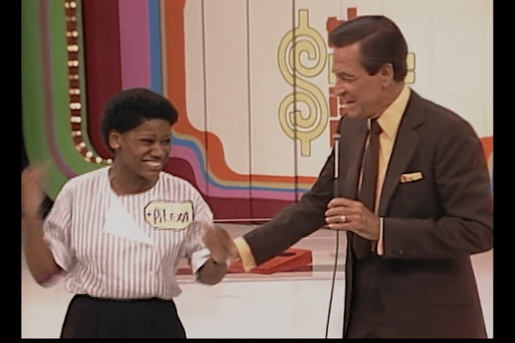 A contestant joyfully interacts with the host on stage during a game show, with vibrant set design in the background.
