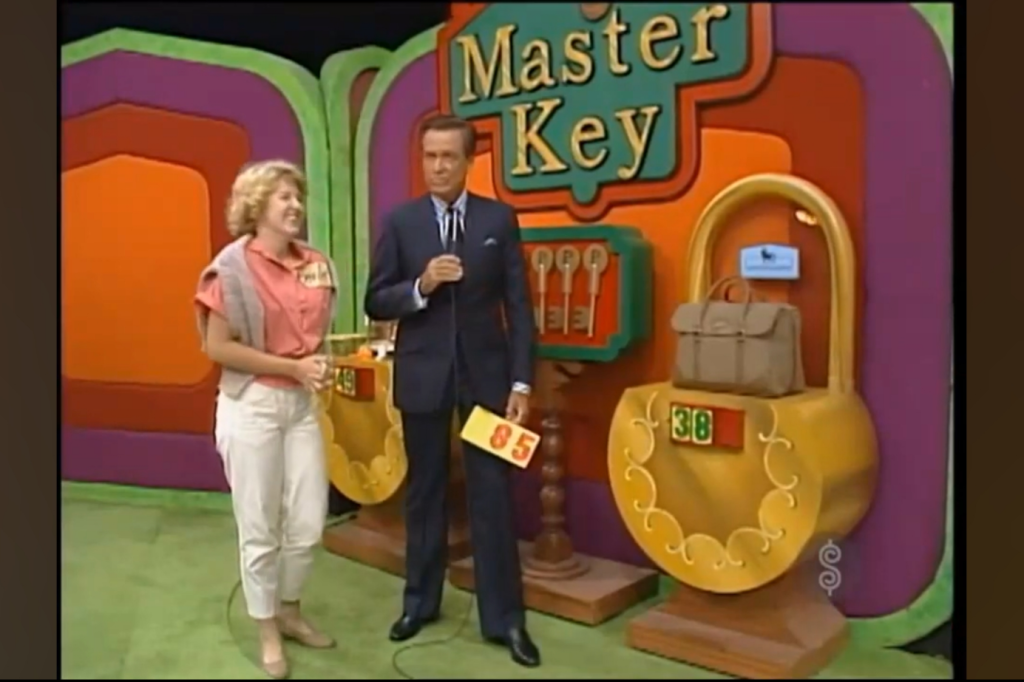 A female contestant smiles next to a male host, both standing in front of the Master Key game setup with colorful backgrounds and a large lock displaying a prize.