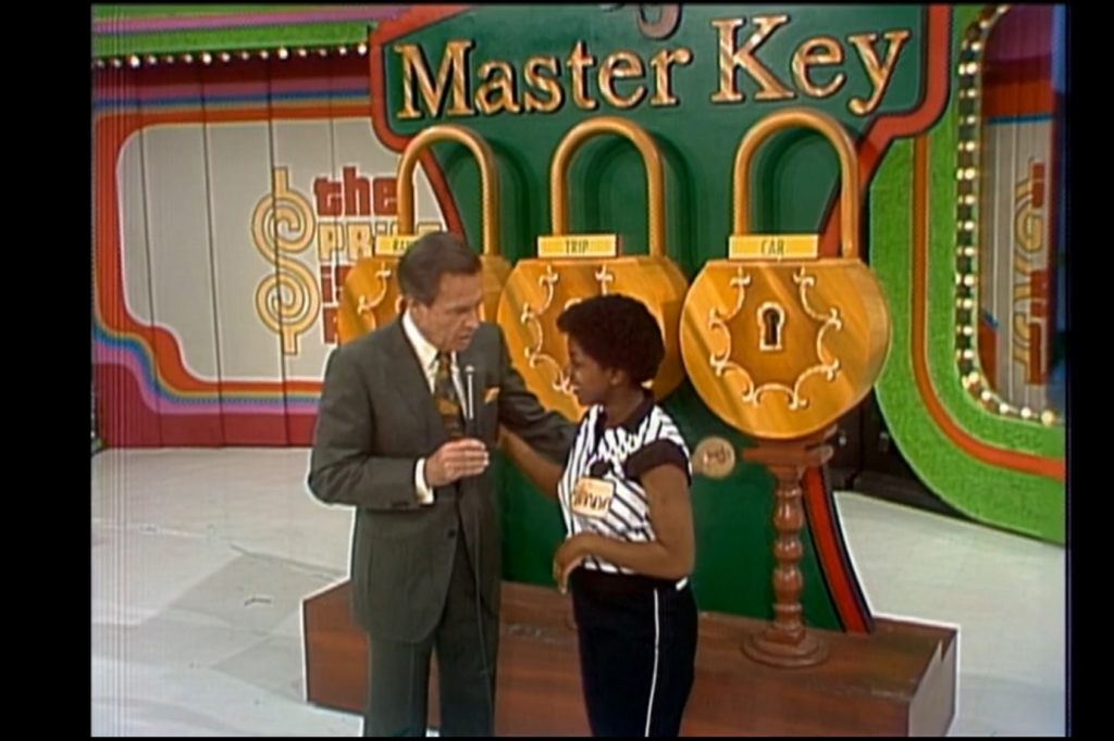 A contestant interacts with the host in front of the Master Key game setup, featuring three large locks and a colorful background.