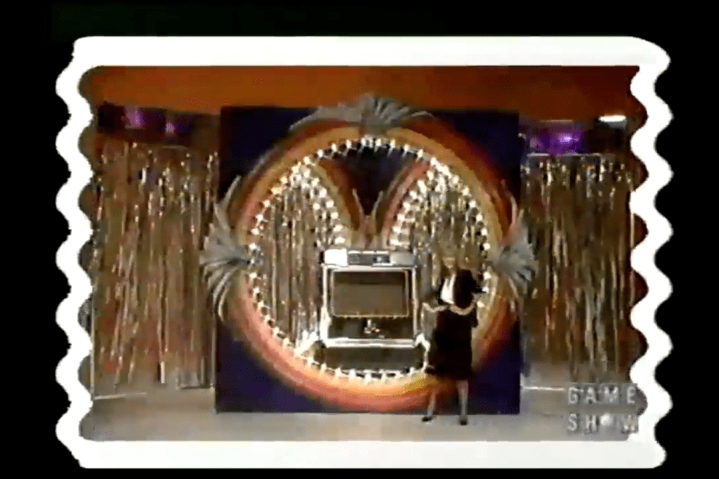 A game show set featuring a large colorful backdrop with a jukebox displayed, and a model standing beside it.