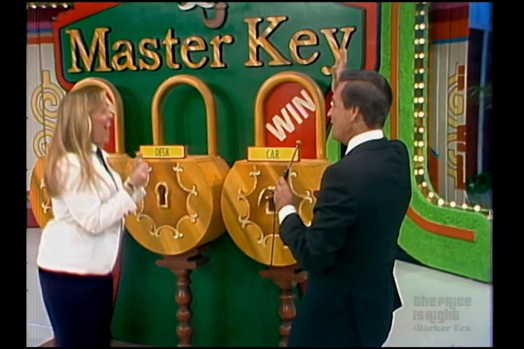 A contestant celebrates as they stand next to two large locks labeled 'DESK' and 'CAR' on the set of the Master Key game on The Price is Right, with the Master Key sign prominently displayed in the background.
