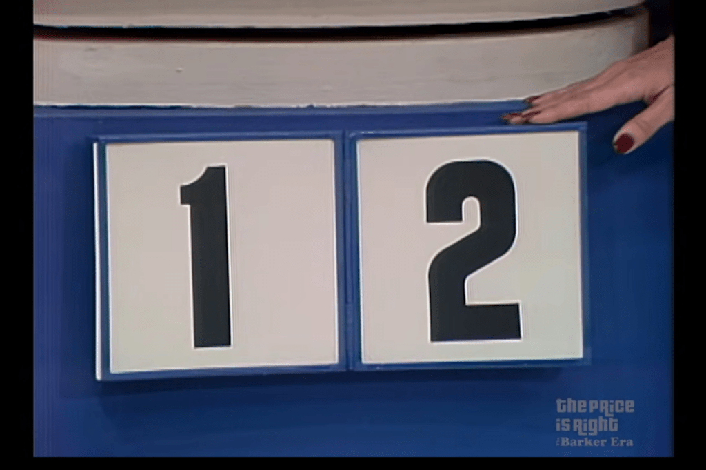 A blue game board displaying the numbers '1' and '2' on large white cards, with a hand partially visible holding the card for '2'.