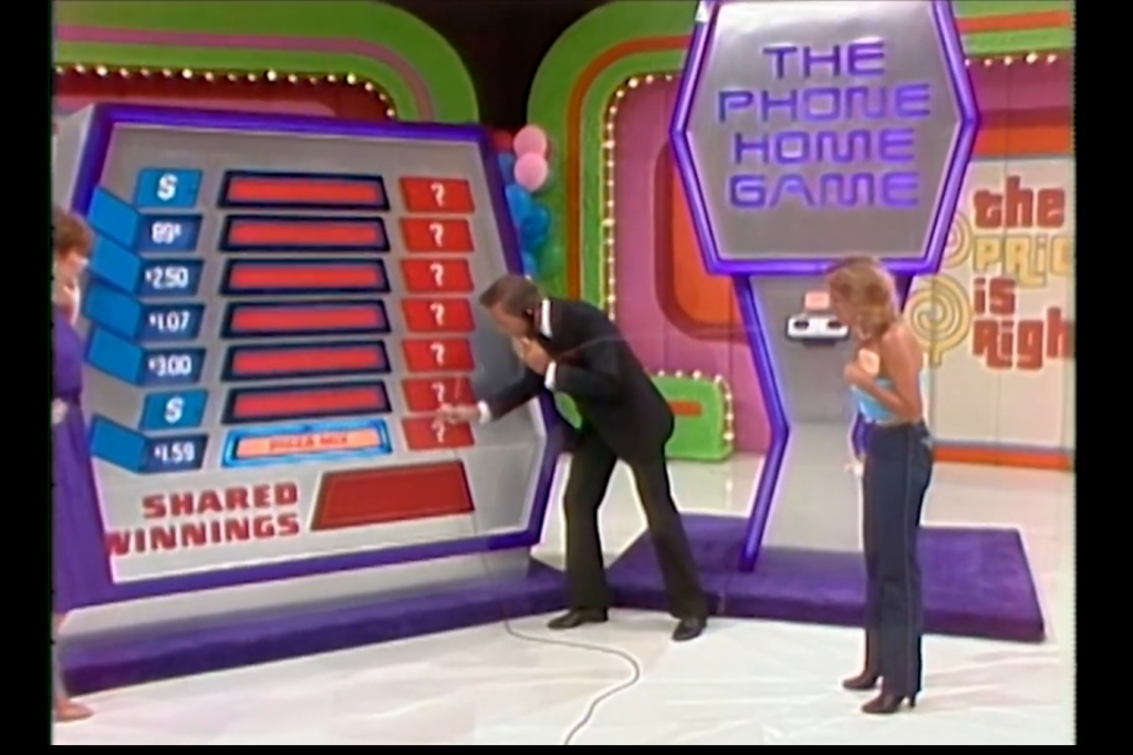 A host reveals the prices behind red and blue doors in The Phone Home Game on The Price is Right, with contestants eagerly watching.