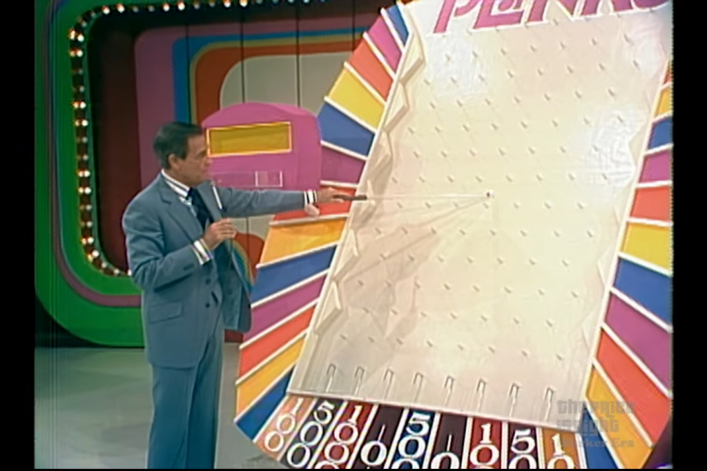 Bob Barker brandishing his 'Plinko stick' to retrieve stuck Plinko chips from the Plinko board.