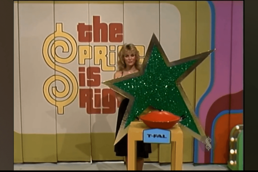 A female model stands beside a large glittery green star and an orange bowl labeled 'T-FAL' on the set of 'The Price is Right.'