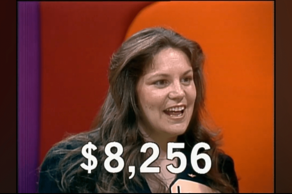 A contestant smiles and celebrates, with a score of ,256 displayed in front of her.