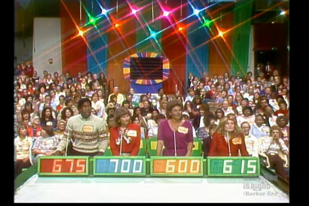 A blacked-out Plinko board masked in the back of the audience as contestants bid.