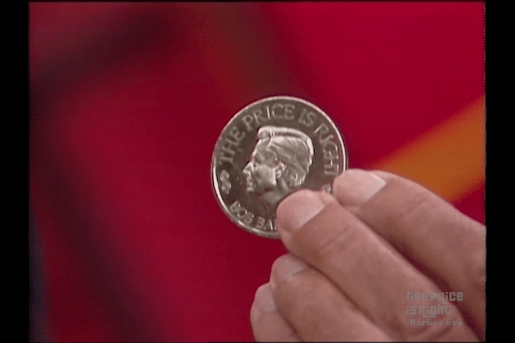 A close-up of a Barker Silver Dollar from the game show 'The Price is Right' held in a person's hand, with a blurred background.
