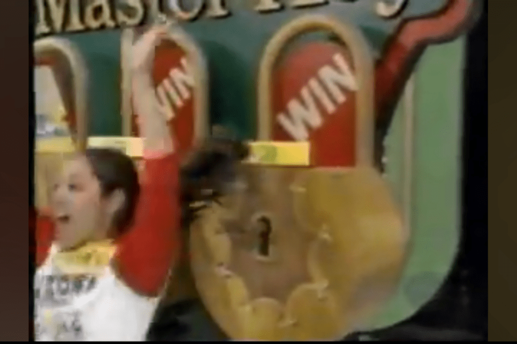 A contestant celebrating with raised arms in front of three locks labeled 'WIN' during the Master Key game.