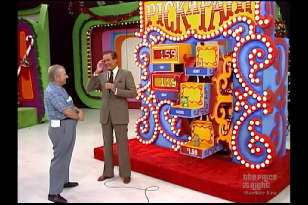 Contestant standing with host at the 'Pick a Pair' game board in a colorful studio setting, with prices displayed.