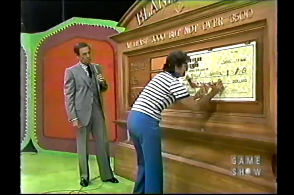 Contestant filling out a large novelty check while a host stands nearby, during a The Price is Right.