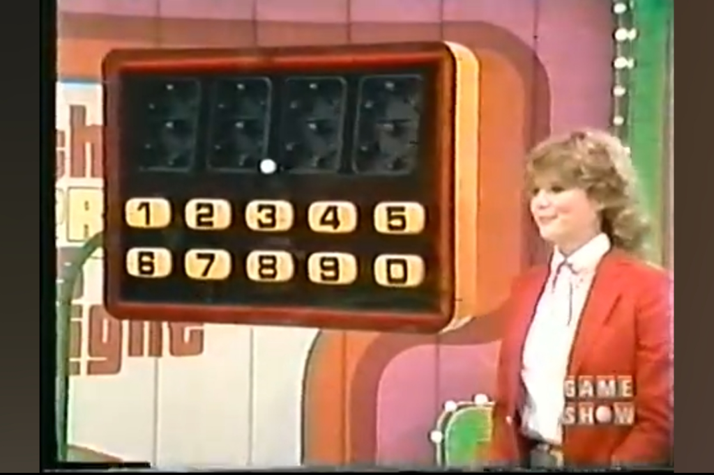 Model Holly Hallstrom stands next to a giant calculator with numbers 1-9 and a mechanical display for The Price is Right game, Check-Out, in a colorful game show setting.