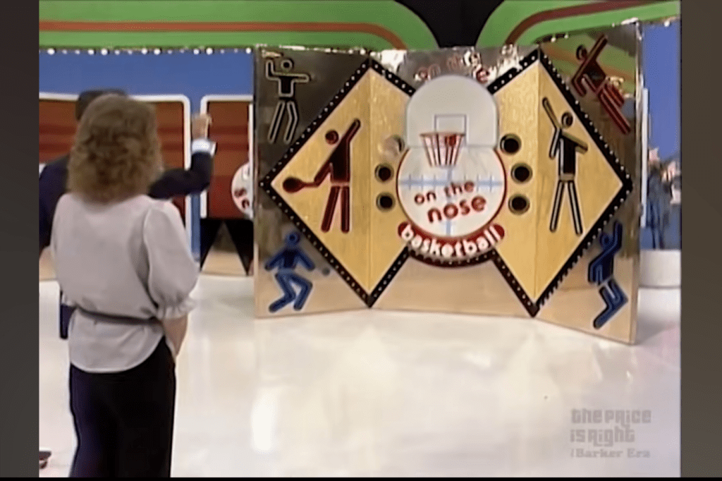 A scene from the game show 'On the Nose' featuring a contestant pointing at a colorful game board with basketball-themed graphics.