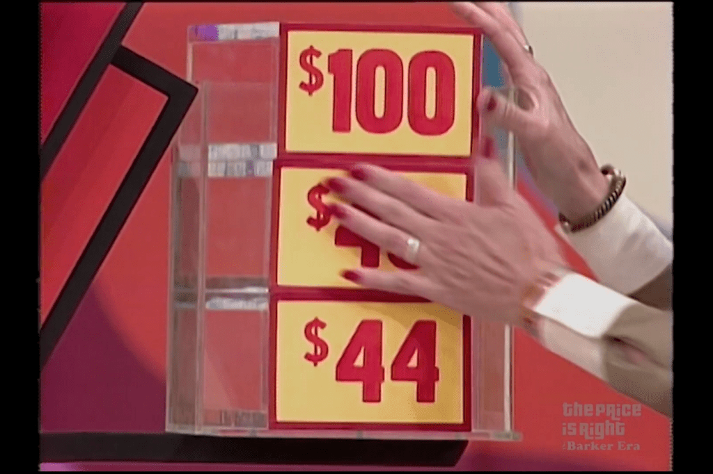 A hand is shown touching a vertical display with three price tags, reading 0, , and , against a colorful background from The Price is Right.