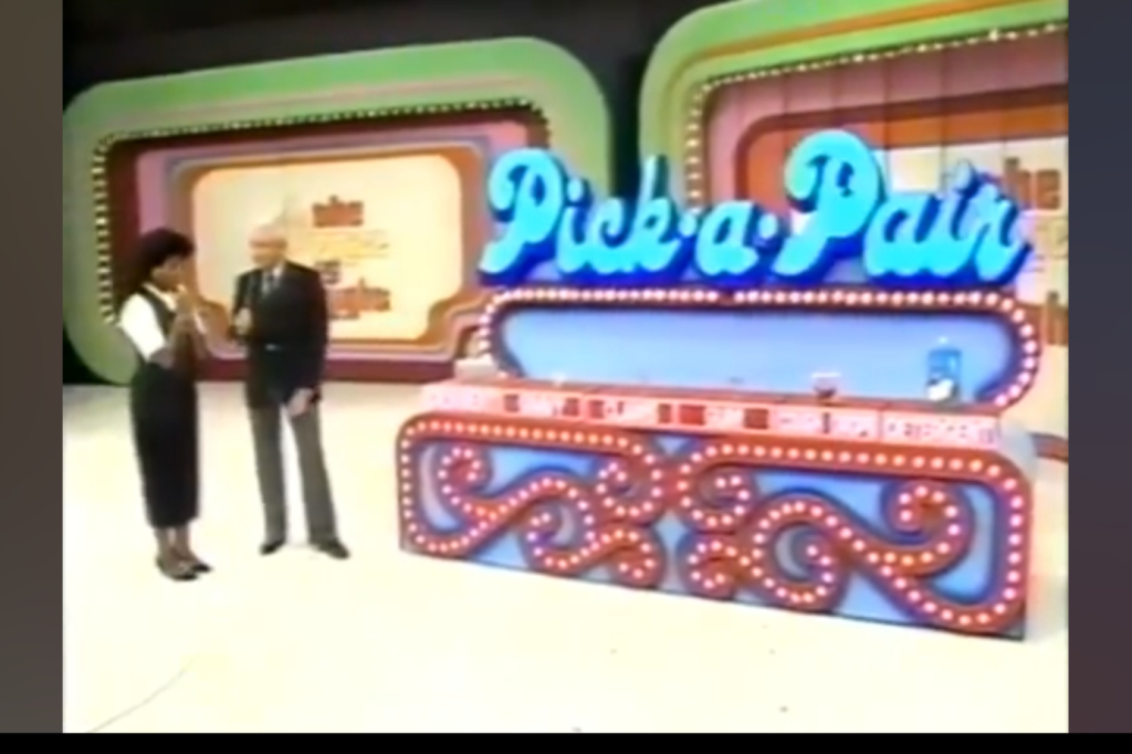 A host and a contestant are engaged in a game show called 'Pick a Pair,' featuring colorful set design and illuminated letters.
