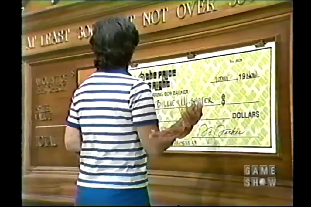 A contestant fills out a large novelty check for a pricing game on The Price is Right, aiming for a winning total.