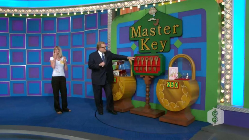 A game show host points at a display with various keys and locks for the 'Master Key' game, while a contestant expresses excitement in the foreground.