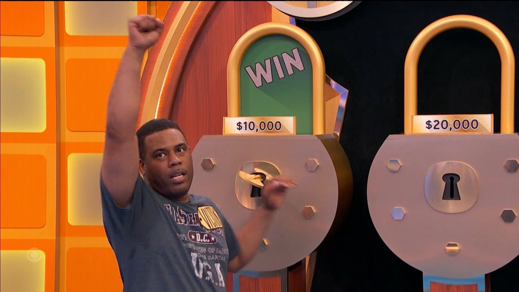 A contestant celebrates while raising their arm in excitement next to two large locks, one displaying a prize of ,000 and the other ,000, in the game show Master Key.
