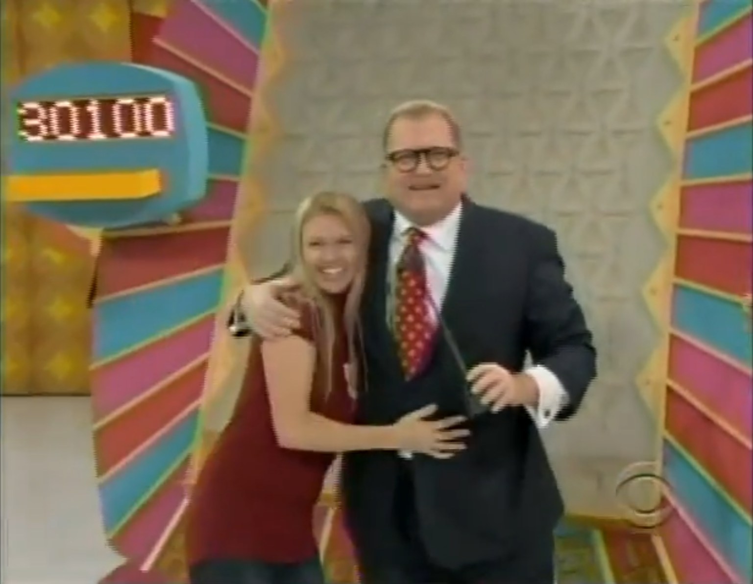 A contestant celebrates with The Price is Right host Drew Carey after winning ,100 on the Plinko game, surrounded by colorful game show decor.