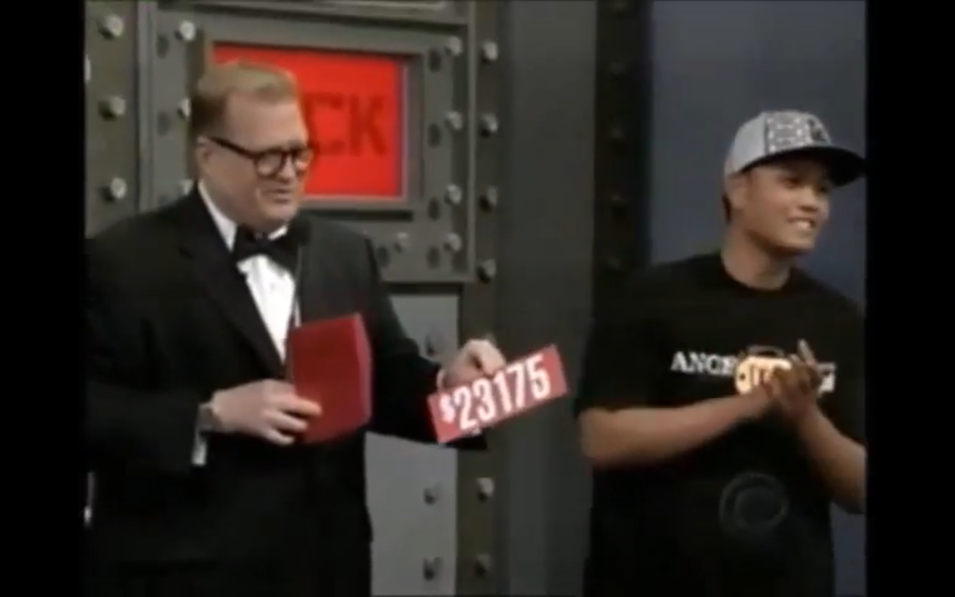 A host from The Price is Right holds a price tag of ,175 while a contestant smiles and claps beside him, standing in front of a large safe backdrop.