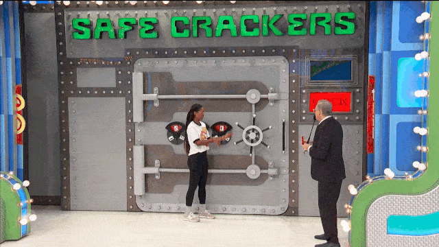 A contestant interacts with a large, grey safe on The Price is Right, while Drew Carey knocks a light bulb out of the socket.