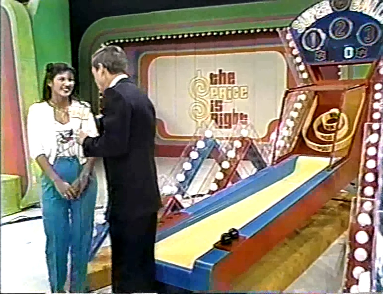 A contestant smiles while speaking with the host of The Price is Right in front of the Super Ball game ramp, featuring colorful lights and a prominent logo.