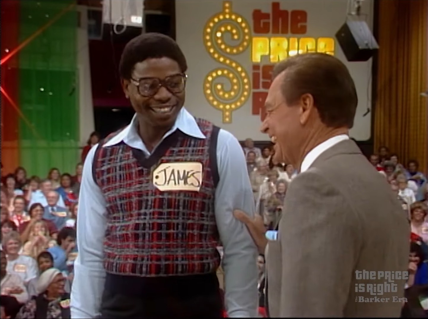 A contestant named James smiles while interacting with host Bob Barker on the set of The Price is Right, with a colorful audience in the background.