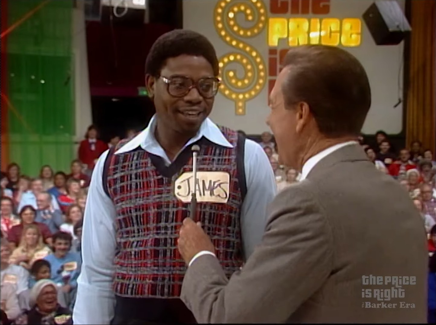 A contestant named James stands on stage during The Price is Right, speaking to the host Bob Barker with an audience in the background.