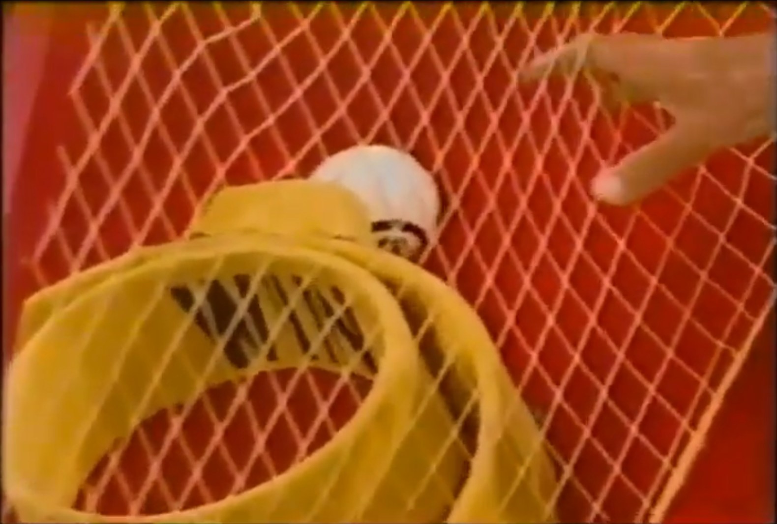 A close-up view of a yellow netted goal in Super Ball with a white ball partially obscured, and a hand reaching towards it on The Price is Right.