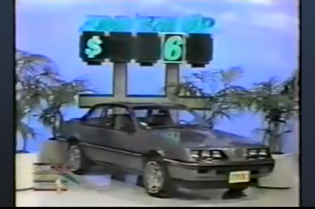 A gray Pontiac Sunbird Coupe is displayed with the Add 'Em Up game board showing the partial price '$__6' in a game setting.