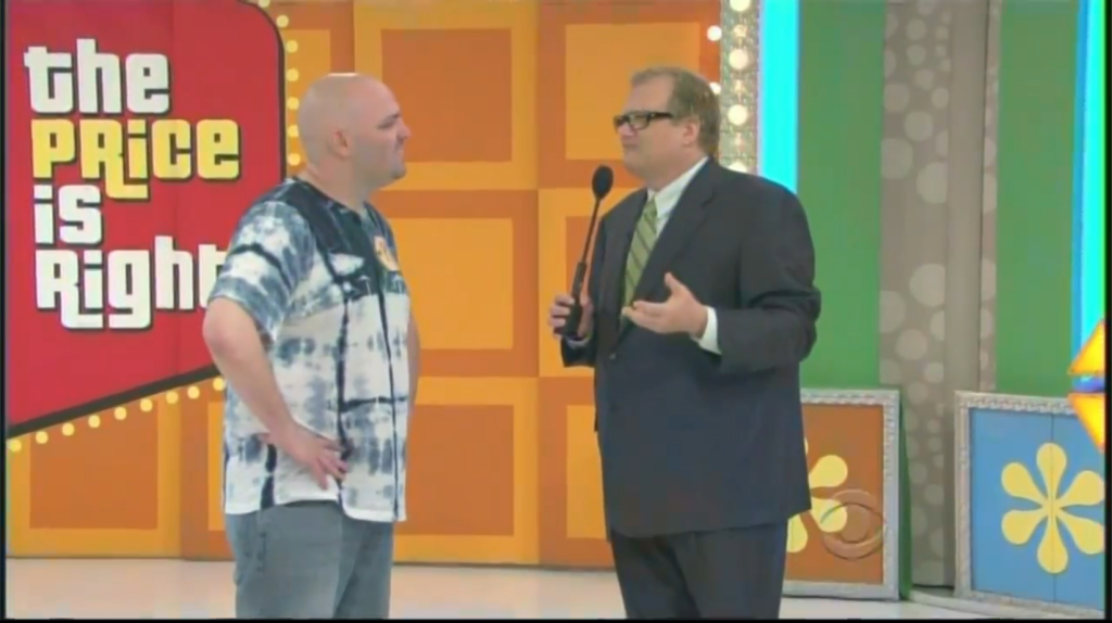 Drew Carey and a contestant interact on stage during a game show segment, with a vibrant background featuring the show's logo.